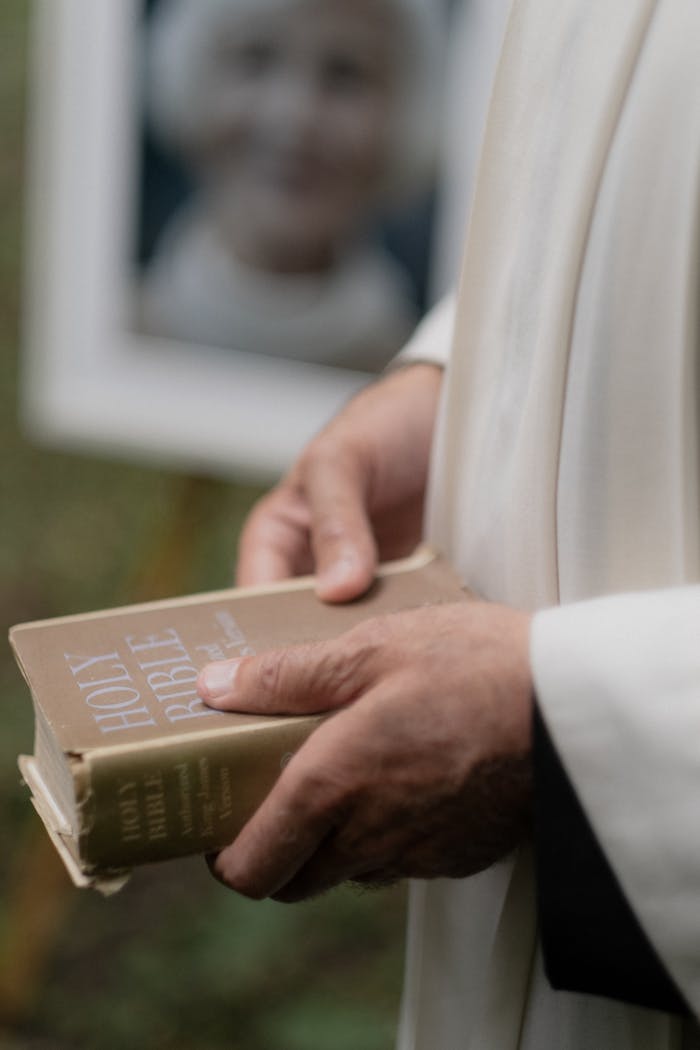 Crafting Captivating Headlines: Your awesome post title goes here A close-up of a priest holding a Bible during a funeral ceremony outdoors.